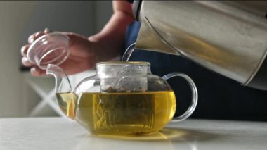 Mutfakta bir çaydanlığı yeşil çay için çaydanlıktan çıkan sıcak suyla dolduran bir kız.