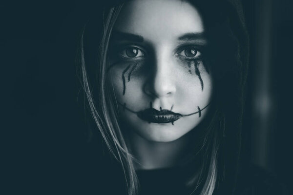 Little girl with spooky Halloween makeup looking at camera. Creepy kids portrait in black and white.