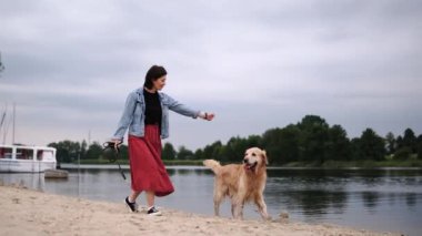 Kız, kumsalda sevimli, altın bir köpekle yürüyor.