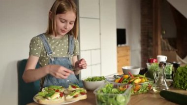 Şirin bir yer ve küçük bir kız akşam yemeği için sağlıklı sandviç ve salata yapıyor.