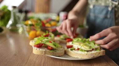 Kahvaltı için sağlıklı sebzeli sandviçler hazırlayan genç kız, peynirli, avokadolu ve domatesli.
