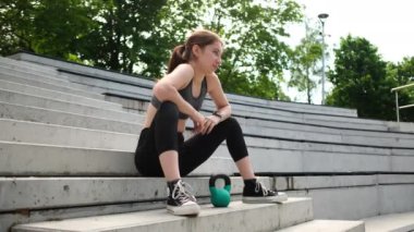 Parkda kettlebell ile spor yapan formda kız vücut geliştirmeye odaklanıyor.