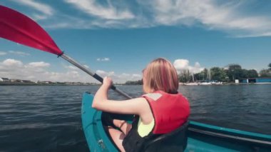 Can yeleği giymiş, gölde kano süren açık hava su sporlarının tadını çıkaran küçük bir kız.