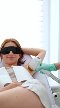 Doktor, güzellik kliniğindeki kadın koltukaltlarına lazer cihazı takıp vücut kıllarını aldırıyor.