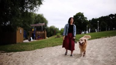 Kız, kumsalda sevimli, altın bir köpekle yürüyor.