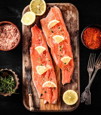 Biberiyeli taze alabalık fileto ve ahşap tahtada limon, baharatlar ve pembe tuzla servis edilmeye hazır. Omega portakal balığı ve turunçgiller sağlıklı beslenme için.