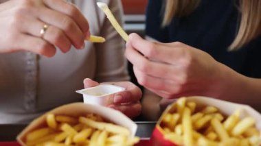 Anne ve küçük kızı fast food lokantasında sosla patates yiyorlar.