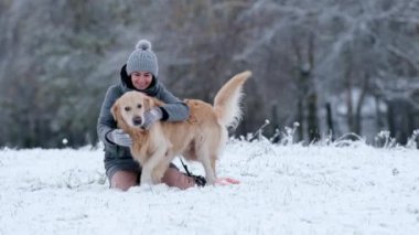 Kışın kar yağarken altın av köpeğini okşayan kız.