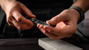 Katlanmış bıçaklı ve bilenmiş taş aletli bir adamın elleri. Değirmen taşında çakı keskinleştirme ustası