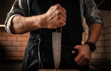 Şef önlüklü adam mutfakta dikey bıçak tutuyor ahşap döşeme tahtasıyla oynuyor. Lokanta proffesional mutfak aracı yakın çekim