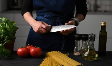 Woman In Chief Apron checking a Sharpening knife Preparing To Cook Spaghetti clipart