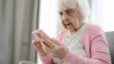 Yaşlı Kadın Akıllı Telefon Ekranını Kaydırıyor ve Sosyal Medya Beslemesini Çevrimiçi Okuyor