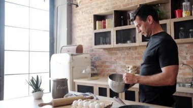 Genç adam kasede yumurta sallarken mutfakta yemek pişiriyor.