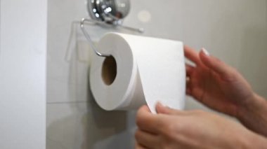 Kadın bir parça tuvalet kağıdını yırtıp, tuvalete sarkıyor.