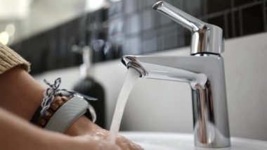 Kız banyoda sabunla ellerini yıkıyor, mikser musluğundan sıcak su dökülüyor, yakın çekim görüntüsü...