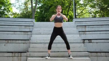 Spor ve vücut geliştirme için dışarıda çömelme yapan genç kız bacaklarına odaklanıyor.