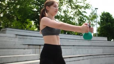 Parkta spor yapan, ağırlık kaldıran ve Kettlebell egzersizlerini kadın vücut geliştirme rutininin bir parçası olarak yapan sağlıklı bir kız.