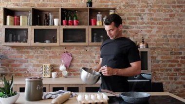 Genç adam mutfakta omlet pişiriyor, sağlıklı bir sabah kahvaltısı için kasede yumurta sallıyor.