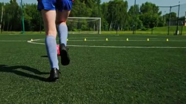 Küçük futbolcu antrenman sırasında yeşil sahada topla koşuyor.