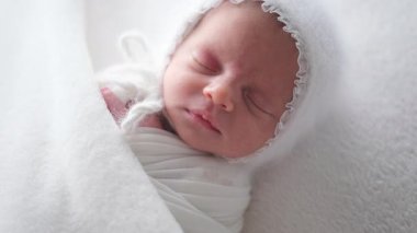 Yeni doğmuş şirin bir kız bebek, battaniyeye sarılmış ve tatlı bir şekilde uyuyan bir şapka giyiyor.