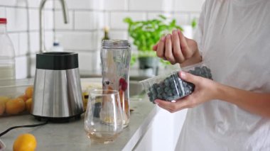 Küçük kız mutfakta milkshake 'e yaban mersini ve ahududu ekliyor.