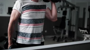 Spor salonunda ağırlık kaldıran, güç ve dayanıklılık için kollarını çalıştıran bir adam.