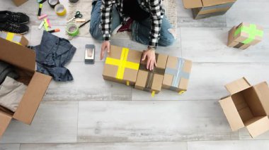 Kız, karton kutuları toplar, fotoğraf çeker, paketleri nakliyeye hazırlar.