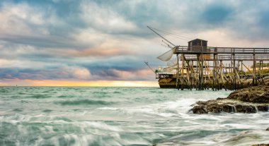 Geleneksel balıkçı kulübesi, Fransa kıyılarında balık ağıyla birlikte. Plajda balık tutmak için tipik ahşap evler.