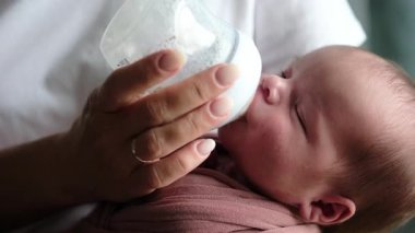 Anne, evde bebeğe bakarken yeni doğan bebek maması ile bir şişeden besleniyor.
