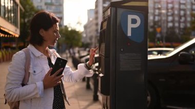 Şehir merkezindeki kadın sürücü bir park sayacı makinesinin plakasını yazıyor.