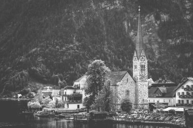 Avusturya 'nın Hallstatt kentindeki göl ve dağ manzarasında güzel bir Protestan kilise saat kulesi manzarası. Siyah beyaz fotoğraf.