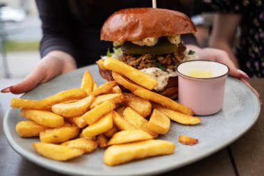 Elinde bir tabak kızarmış patates ve bir lokantada et burgeri tutan bir kız.