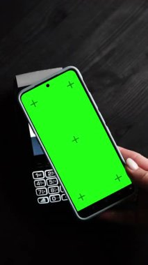 Terminalde yeşil renkli anahtar ekranlı akıllı bir telefonla ödeme yapan ve tasarımınız için ekranda, dikey bir videoda boşluk bırakan bir kız.