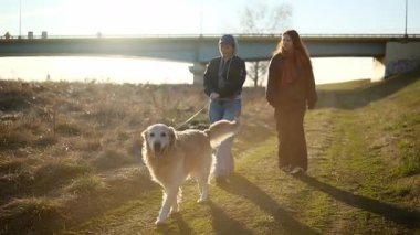 Anne ve kızı gün batımında dışarıda Golden Retriever Dog ile yürüyor.
