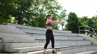 Fit kız parkta egzersiz yapıyor, ağırlık kaldırıyor ve kettlebell kullanıyor.