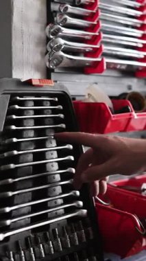 Adam garajda çeşitli aletlerle, dikey videoda rafta bir düğme seçiyor.