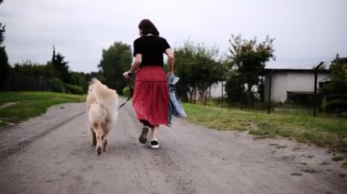 Kırsal bir yol boyunca sevimli Golden Retriever 'la koşan bir kadın köpekle oynuyor.