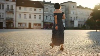 Açık renk elbiseli genç bir kadın gün batımında bir Avrupa şehrinin tarihi bölgesinde yürüyor.