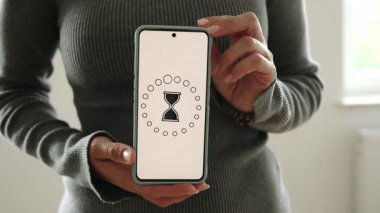 Kız, yükleme işlemi ve beyaz ekranda dönen bir kum saati simgesi olan akıllı bir telefon gösteriyor