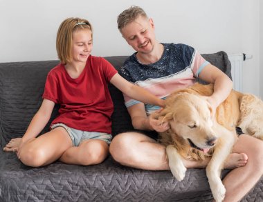 Baba ve kızı evdeki koltukta köpeği okşadı.