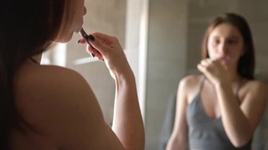 Kız dişlerini banyoda fırçalıyor ve sabahları aynaya bakıyor.