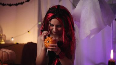 Cadılar Bayramı Cadısı 'ndaki şirin küçük kız bir balkabağıyla oynuyor, ürkütücü bir yüz çiziyor ve onu bir hayalete gösteriyor.