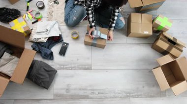 Kız karton kutular içinde giysiler ve her kutuda bant var.