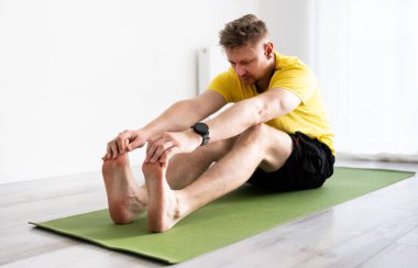 Sportif Genç Adam Yoga yapıyor ve evde yerde otururken çekirdek esnetiyor.