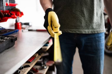 Otomobil tamircisi garajda bir mezura tutuyor.