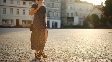 Açık renk elbiseli genç bir kadın gün batımında bir Avrupa şehrinin tarihi bölgesinde yürüyor.
