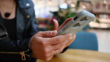 Bir ticaret merkezinde mesajları ve sosyal medyayı kontrol etmek için akıllı telefon kullanan genç bir kadın.