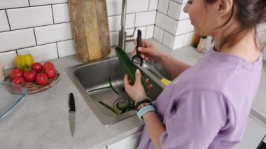 Mutfakta bir kadın taze sebze salatası için salatalık soyuyor.