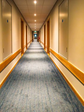 Otel koridorunda ışık ve kapılı liminal alan yok. Sona giden gri halı.