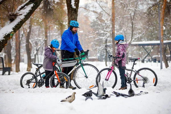 A man with his son and daughter ride bicycles in a winter park. Father with children. Winter weekend